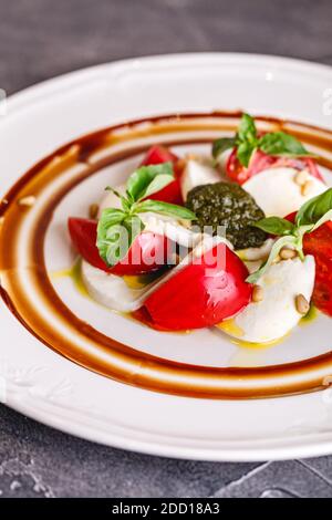 Caprese salad with mozzarella, tomato, basil and pesto arranged on white plate Stock Photo