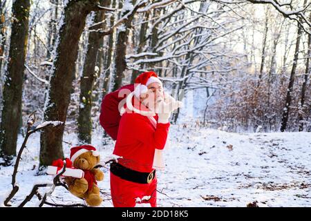 Santa Claus walking to the winter forest with a bag of gifts, blow snow. Happy New Year. Stock Photo