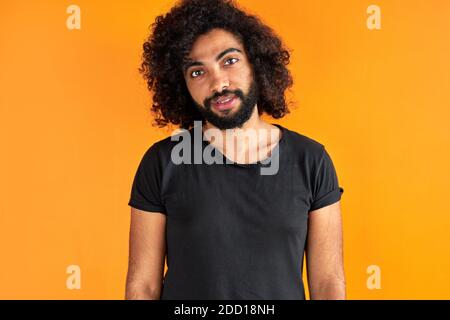 portrait of pleased arab man isolated in studio, handsome guy in casual wear posing at camera, has black long curly hair, calm male of indian or arabian appearance Stock Photo