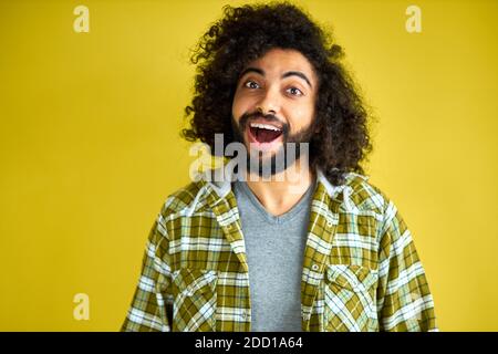young arab man is shocked, show surprise and amazed expression. handsome guy with long curly hair and beard stay in shock, isolated on green background Stock Photo