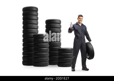 Auto mechanic with a car tire and piles of tires behind isolated on white background Stock Photo