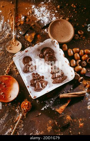 Christmas chocolate figures Santa Claus, Christmas tree, bells, candle are on the dark table next to a chocolate bar with orange and spices Stock Photo