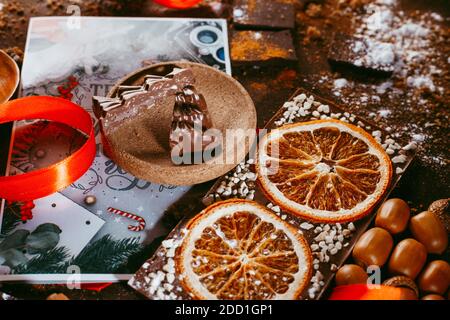 Christmas chocolate figures Santa Claus, Christmas tree, bells, candle are on the dark table next to a chocolate bar with orange and spices Stock Photo