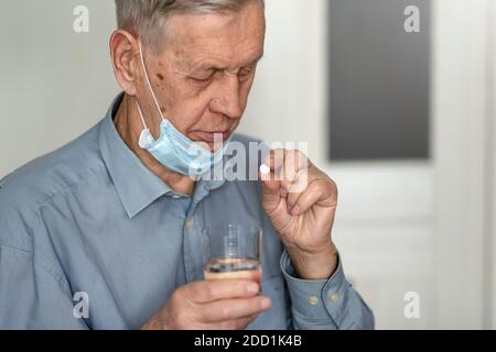 An elderly man in a medical mask takes a pill. Health problems in old age, aging process. Stock Photo