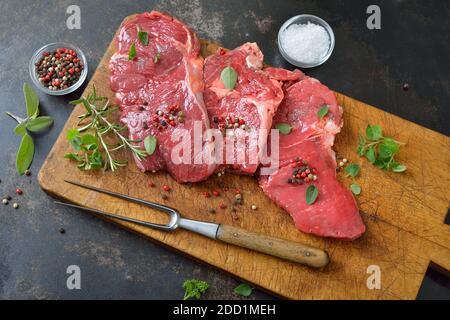Three raw rib eye steaks with spices and herbs on an old wooden cutting board Stock Photo