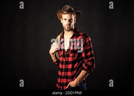 Cowboy wearing hat hold rope. Lasso tool of American cowboy. Still used on ranches to capture cattle or other livestock. Western life. Lassoing on prairie. Man unshaven cowboy black background. Stock Photo