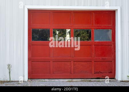A wooden garage door painted red with glass windows and metal handles is surrounded by a white wall. Stock Photo