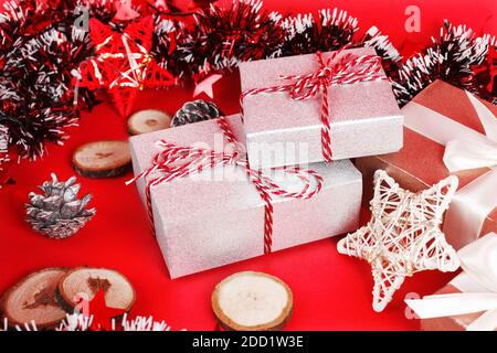 Gift boxes wrapped in glitter silver paper and red stripprd ribbon on a red background among christmas decorations. New year concept. Holiday event st Stock Photo