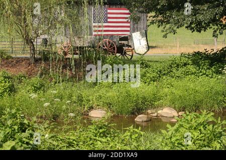 Virginia, USA. American flag displayed on an wooden shed. Old cart with flag used as yard decor. Stock Photo