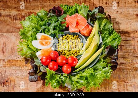 Green vegetable salad with salmon chicken eggs avocado tomatoes green lettuce on a wooden backgraund Stock Photo