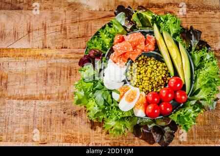 Green vegetable salad with salmon chicken eggs avocado tomatoes green lettuce on a wooden backgraund Stock Photo