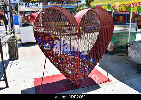 A unique red heart shaped trash can / bin for the collection of plastic bottle tops and caps at a small fun fair along the Malecon in Progreso, Mexico. Stock Photo