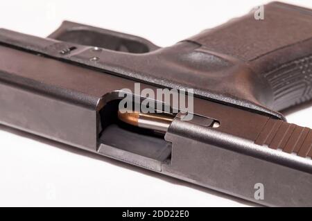 A black 9mm pistol with an open slide showing a bullet about to be chambered on a white background Stock Photo