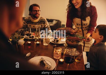 Woman serving roasted turkey to family. Female serving thanksgiving turkey for family dinner at home. Stock Photo