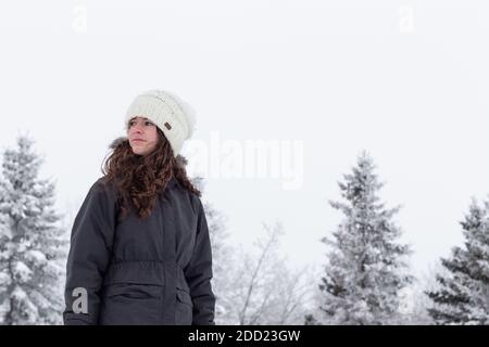 Young adult, beautiful teen girl, wearing winter clothes standing outside with frost and snow on trees MR Images of people with lots of copy space Stock Photo