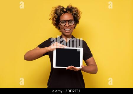 Happy young african lady holding a tablet computer showing empty screen. Studio shot. Stock Photo