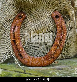 rusty horse shoe leaning against burlap on wood porch Stock Photo