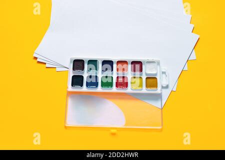 Blank white sheets and 12 colors of watercolor paint on a yellow background Stock Photo