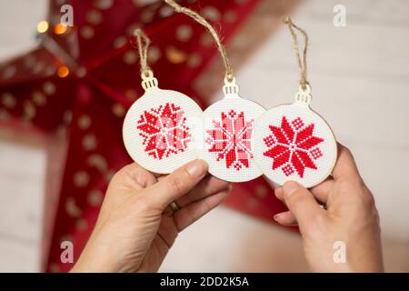 Female hands holding Christmas decoration, big red star in the background. Hand made cross stitch folk Christmas decoration ornament embroidery. Stock Photo