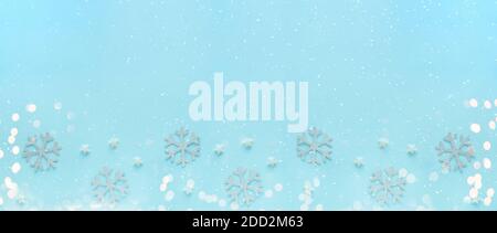 Merry Christmas and Happy Holidays greeting card, frame, banner, flat lay. New Year. Silver ornaments with bokeh and snow on blue surface. Winter Stock Photo