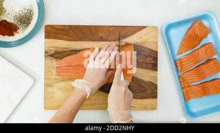 Woman cuts salmon on wooden cutting board. Smoked paprika roasted salmon recipe preparation process. Stock Photo