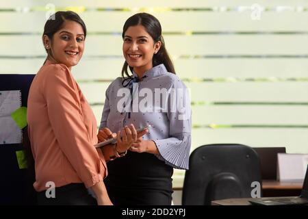TWO EXECUTIVES LOOKING AT CAMERA AND SMILING WHILE WORKING TOGETHER Stock Photo