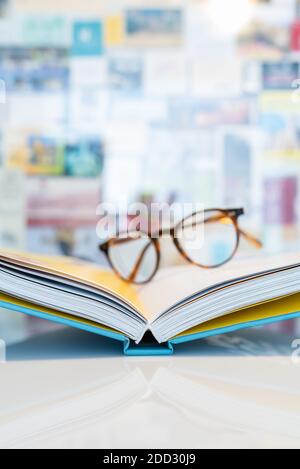 Open book lying on white table with soft blurred reading glasses in background Stock Photo