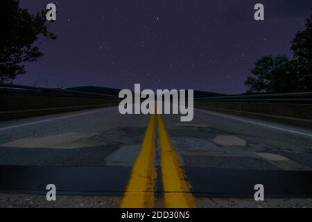 A Low Angle Shot of a Road at Night With Trees on Each Side and Stars in the Sky Stock Photo