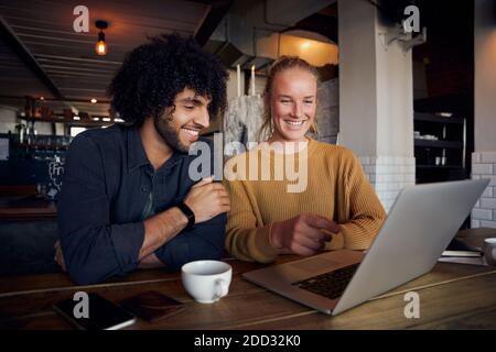 Handsome young man with beautiful woman looking at laptop screen in cafe and drinking coffee Stock Photo