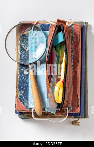 Protective mask, pencil case and magnifying glass on white background. Pandemic limitation Stock Photo