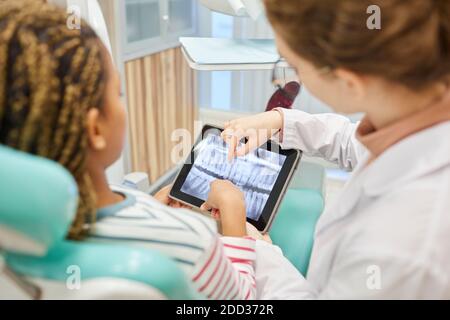 Rear view of patient and doctor examining the x-ray image on digital tablet at dental clinic Stock Photo