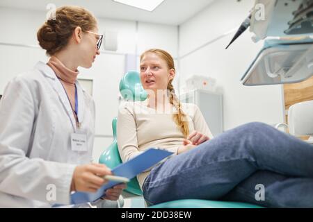 Female patient sitting on dental chair and discussing medical procedure together with dentist at clinic Stock Photo