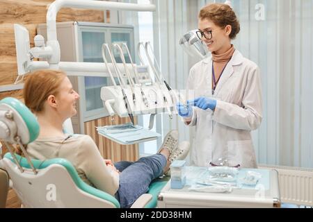 Young dentist preparing her instruments to medical procedure and talking to patient at her office Stock Photo