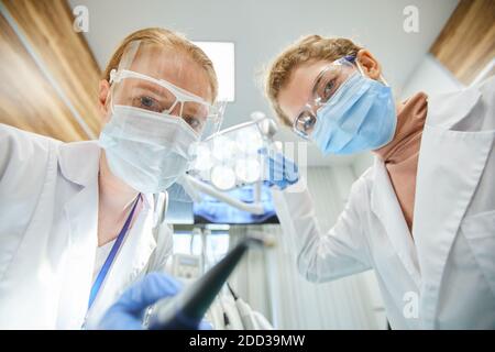 Portrait of two dentists in protective masks and glasses looking at camera while working with medical instruments in team Stock Photo