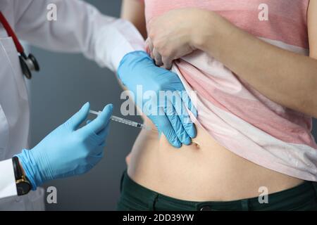 Doctor in rubber gloves making injection into patients skin fold close-up Stock Photo