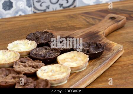 Chocolate coated hazelnut and rice florentines on wood chopping board.  White, milk and dark chocolate selection Stock Photo