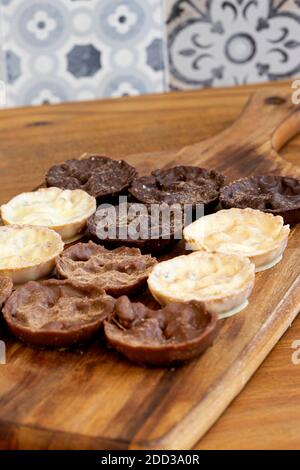 Chocolate coated hazelnut and rice florentines on wood chopping board.  White, milk and dark chocolate selection Stock Photo