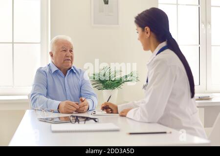 Senior patient consulting young doctor sitting at desk in modern hospital office Stock Photo