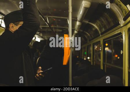 Businessman is commuting on a tram. He is watching something on his smart phone while standing and holding on to the rail. Stock Photo