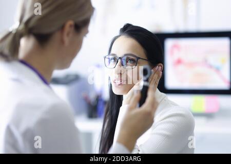 Woman patient holding ear near doctor with otoscope in hand in clinic Stock Photo
