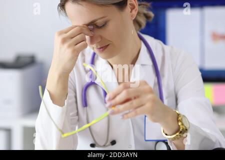 Tired doctor with glasses in hand holding his eyes in clinic Stock Photo