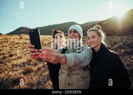 Happy friends bonding together hiking through beautiful mountain terrain taking selfie for social media  Stock Photo