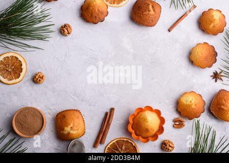 A frame of delicious and fragrant vanilla cupcakes on a light background. Sprigs of pine, cinnamon sticks, orange, nuts, culinary accessories. A place Stock Photo
