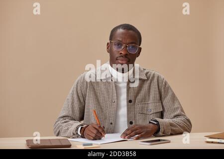 Portrait of African young man in eyeglasses sitting at the table with books and studying Stock Photo