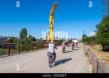 “Ile de Nantes” river island (north-western France): cyclists in the park “parc des chantiers” at the bottom of the yellow Titan crane Stock Photo