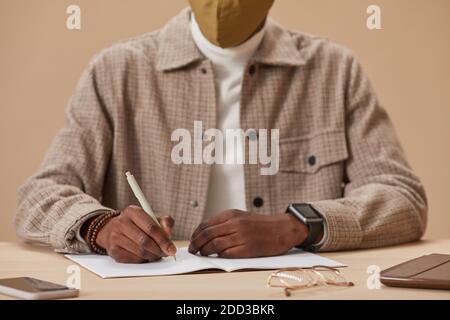 Close-up of man sitting at the table making notes in notebook during online studying Stock Photo