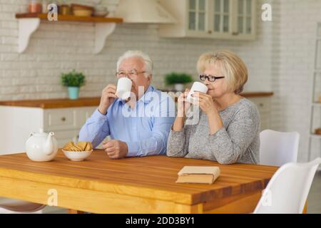 Senior couple with cups in their hands in the morning sitting in the kitchen drinking tea or coffee. Stock Photo