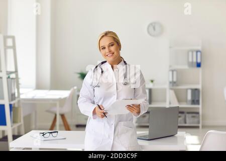 Woman doctor in white medical uniform standing with documents and looking at camera Stock Photo
