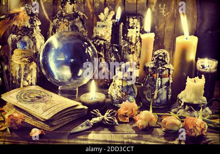 Magic crystal ball, witch bottles and burning candles on the wooden table. Wicca, esoteric, divination and occult background with vintage magic object Stock Photo