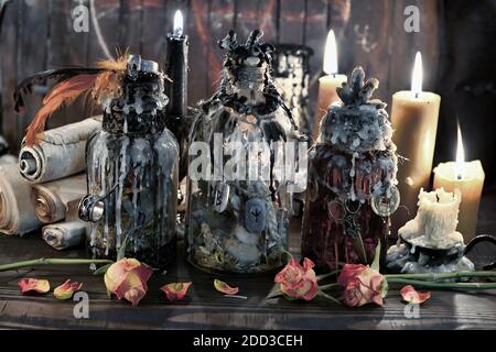 Magic bottles with burning candles, scrolls and flowers on witch table. Wicca, esoteric, Halloween and occult background with vintage magic objects fo Stock Photo
